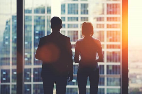 two colleagues looking out of glass window 